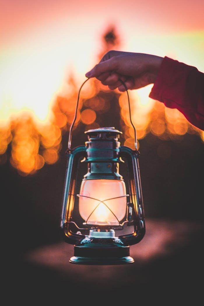 A hand holds a vintage lantern against a bokeh sunset background, creating a warm and nostalgic atmosphere.