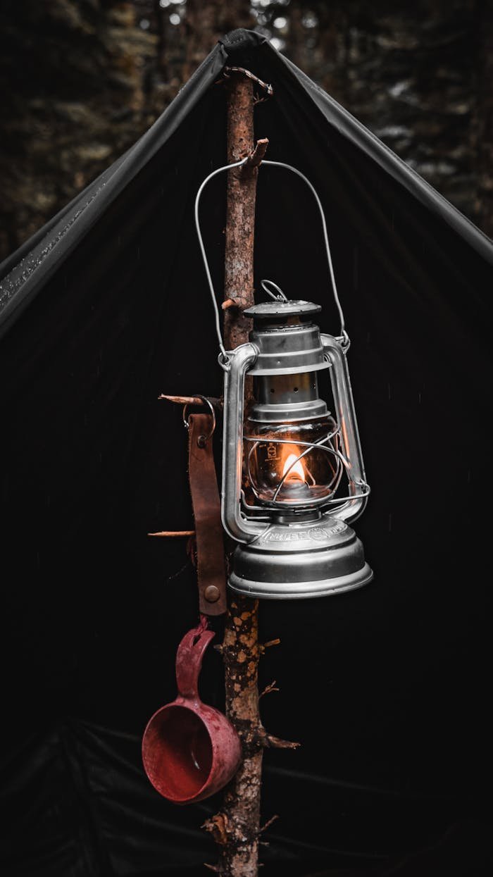 About A vintage lantern hangs on a tent pole, creating a warm glow in a forest camping setting.